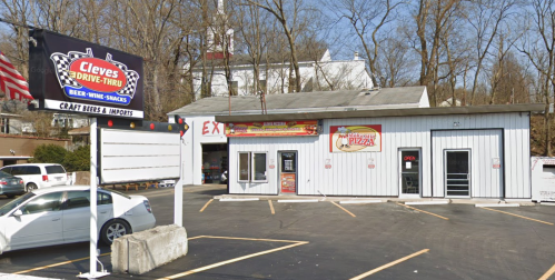 A drive-thru building with a sign for beer, wine, and snacks, featuring a pizza shop, surrounded by trees.