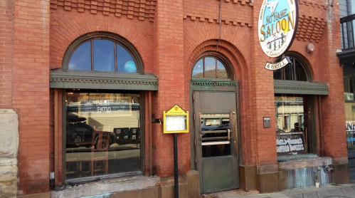 Exterior of a brick building featuring large arched windows and a sign for a saloon and grill.