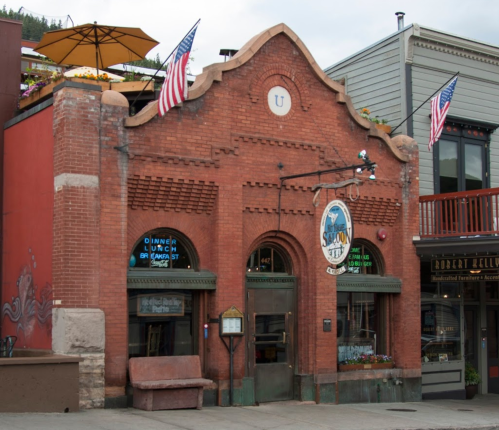 Historic brick building with arched windows, American flags, and a sign for a restaurant in a quaint town.