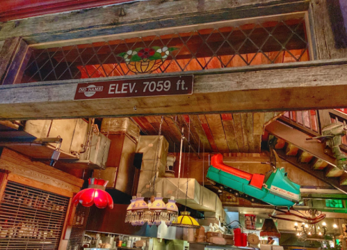 A rustic interior with a sign reading "ELEV. 7059 ft." and vintage kitchen equipment hanging from the ceiling.