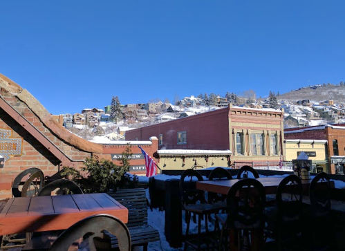 Snow-covered buildings and a clear blue sky in a quaint mountain town, with outdoor seating in the foreground.