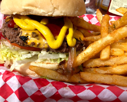 A juicy hamburger with lettuce, tomato, ketchup, and mustard, served with a side of crispy French fries in a red-checkered basket.