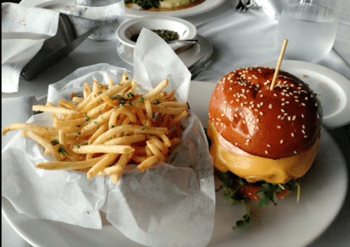 A plate with a cheeseburger topped with lettuce and a side of crispy French fries in a paper-lined basket.