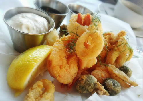 A plate of crispy fried seafood, including shrimp and calamari, served with lemon and dipping sauces.