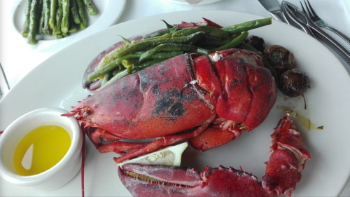A plate featuring a whole red lobster, green beans, asparagus, and a small dish of olive oil.