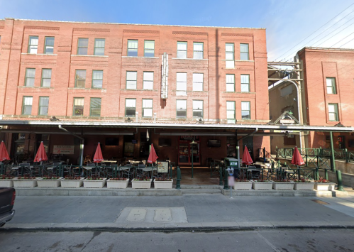 A brick building with outdoor seating and red umbrellas, featuring a restaurant entrance and an ATM nearby.