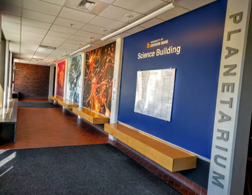 Interior hallway of the University of Southern Maine's Science Building, featuring a "Planetarium" sign and colorful wall art.