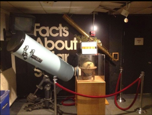 A telescope and a globe displayed in a museum exhibit titled "Facts About Stars." Red ropes cordon off the area.