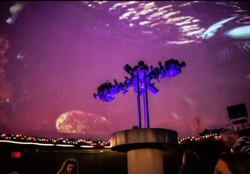 A planetarium projector under a colorful, illuminated dome with a starry projection and festive lights.