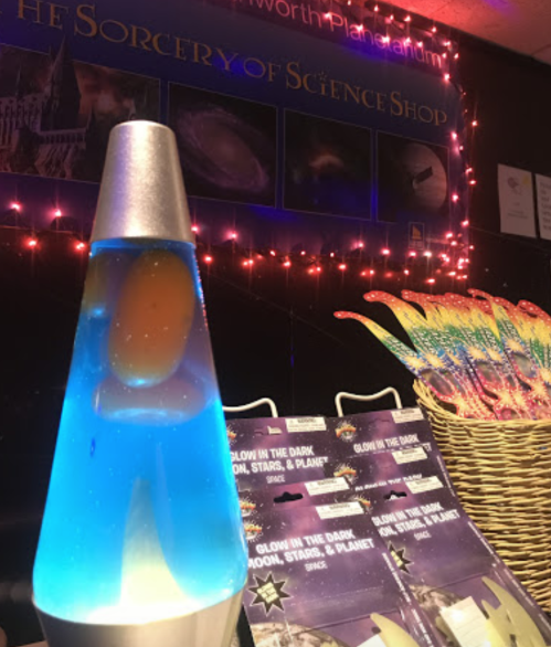 A colorful lava lamp with blue liquid and an orange blob, set against a backdrop of twinkling lights and science-themed decor.