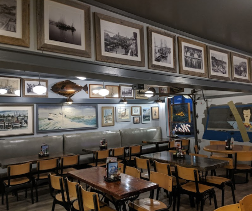 Cozy restaurant interior with wooden tables, chairs, and vintage maritime photos on the walls.