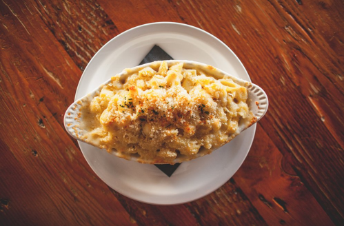 A creamy baked macaroni and cheese dish topped with breadcrumbs, served in a white oval dish on a wooden table.