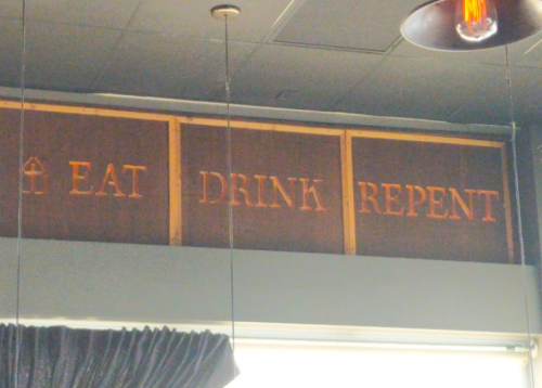Sign on a wall reads "EAT DRINK REPENT" in bold letters, with a decorative arrow above.