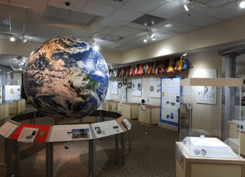 A large globe in a museum exhibit surrounded by informational displays and flags hanging from the ceiling.