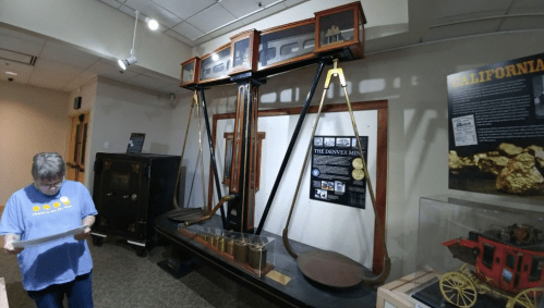 A large vintage scale displayed in a museum, with a visitor examining a document nearby.