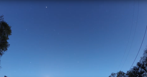 A clear night sky filled with stars, featuring a bright planet and a few scattered clouds.