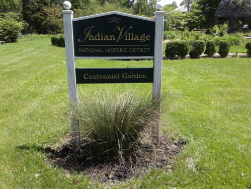 Sign for Indian Village National Historic District, featuring "Centennial Garden," surrounded by green grass and plants.