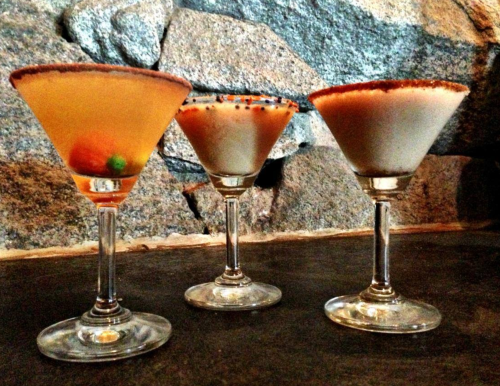 Three colorful cocktails in elegant glasses, garnished and served against a stone background.
