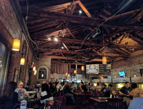 A bustling restaurant interior with exposed wooden beams, dim lighting, and patrons enjoying their meals at tables.