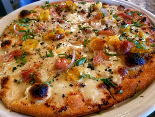 A close-up of a pizza topped with cheese, herbs, and colorful vegetables, served on a white plate.