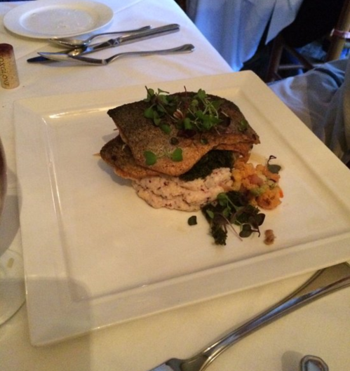 A plated dish featuring crispy fish on a bed of risotto, garnished with microgreens and colorful vegetables.