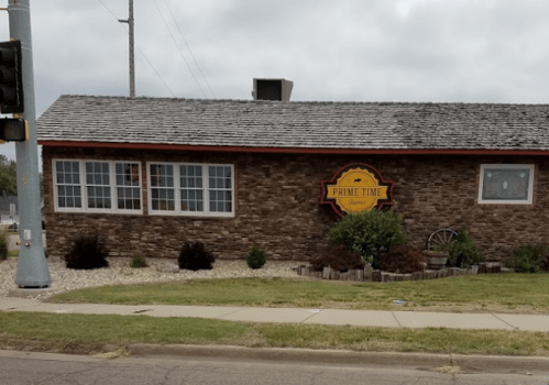 A stone building with a sign reading "Prime Time" and a landscaped yard, viewed from across the street.