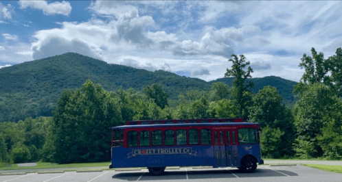 A colorful trolley parked in front of lush green mountains under a partly cloudy sky.