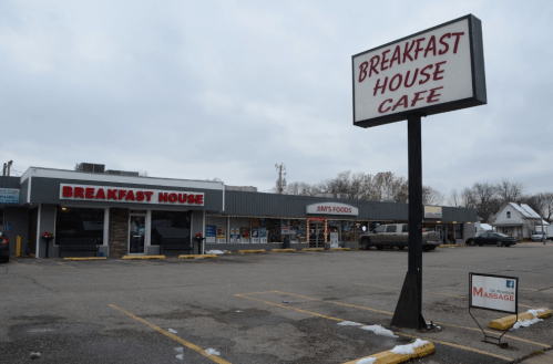 A small shopping plaza featuring a "Breakfast House Cafe" sign, with nearby shops and a massage sign visible.