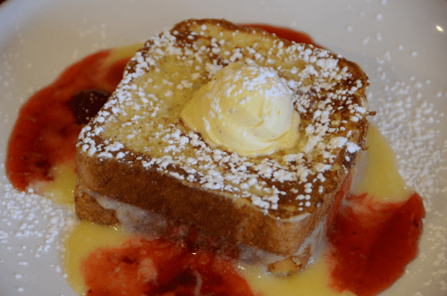 A slice of French toast topped with butter and powdered sugar, served with a drizzle of strawberry sauce.