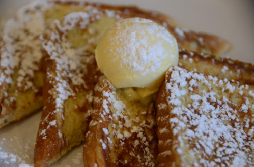 A plate of French toast dusted with powdered sugar, topped with a scoop of butter.