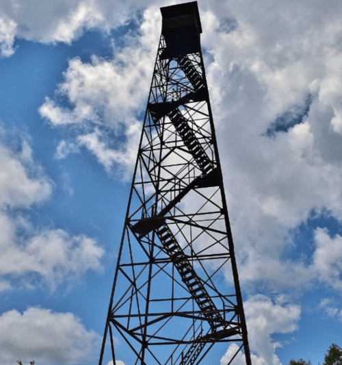 A tall metal tower with a staircase, silhouetted against a blue sky with fluffy white clouds.