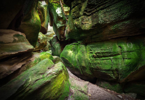 A narrow, moss-covered canyon with towering green rock walls and a winding path through the natural formations.