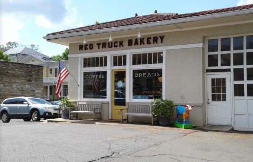 Exterior of Red Truck Bakery with an American flag, benches, and a colorful cow statue outside.