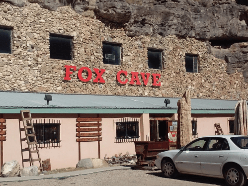 Exterior of Fox Cave building with stone walls, red signage, and a parked white car in front.