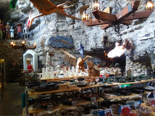 A cave-like shop filled with various crafts, sculptures, and decorations, illuminated by rustic chandeliers.