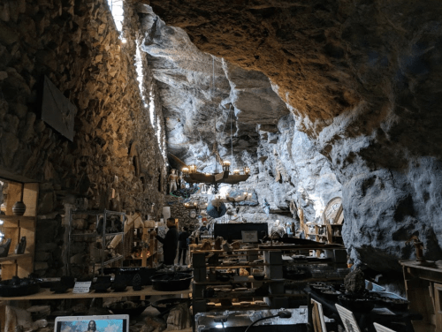A cave interior with stone walls, wooden shelves displaying items, and soft lighting creating a cozy atmosphere.