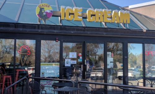 Exterior of Glacier Ice Cream shop with large yellow sign, glass doors, and outdoor seating area.
