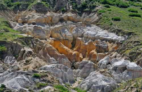 Colorful rock formations and layered hillsides with greenery in a natural landscape.