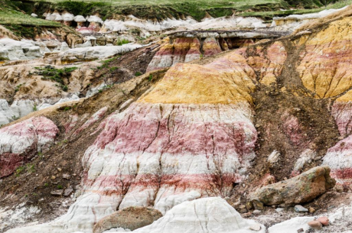 Colorful layered rock formations in shades of red, yellow, and white, set against a green landscape.
