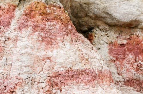Textured rock surface with shades of red and beige, featuring cracks and natural patterns.