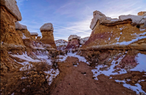 A scenic desert landscape featuring colorful rock formations and patches of snow under a clear blue sky.