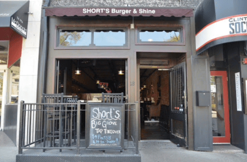 Exterior of SHORT'S Burger & Shine, featuring a sign for a tap takeover and outdoor seating.