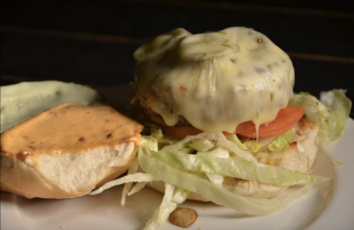 A close-up of a burger with melted cheese, lettuce, tomato, and a side of sauce on a bun.