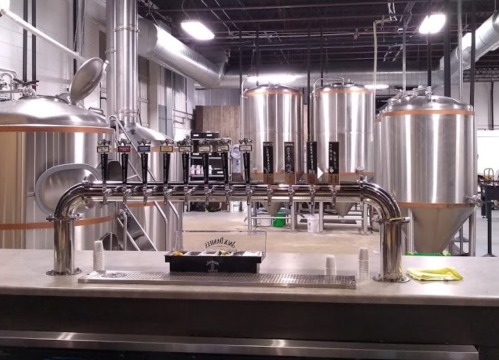 A brewery interior featuring a metal tap system and large fermentation tanks in the background.