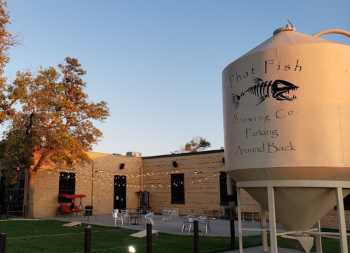 Exterior of Phat Fish Brewing Co. featuring a large brewing tank and outdoor seating area with string lights.