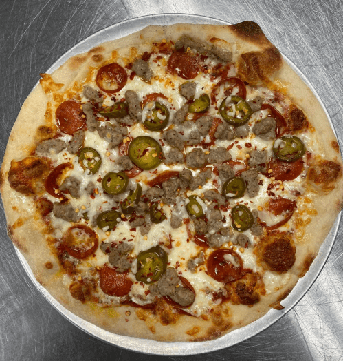 A freshly baked pizza topped with pepperoni, sausage, jalapeños, and sprinkled with red pepper flakes.