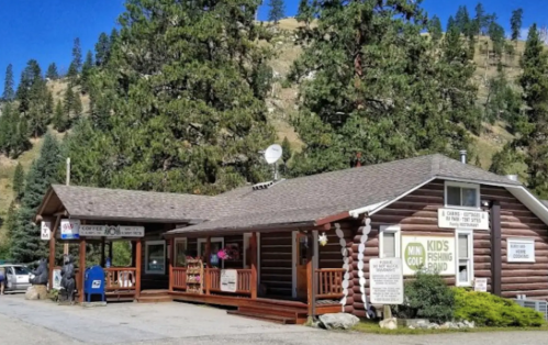 A rustic log cabin building surrounded by trees, featuring signs for fishing and a kids' fishing pond.