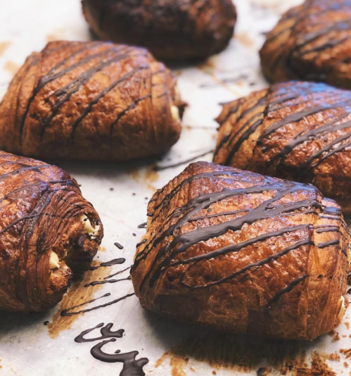 Freshly baked chocolate croissants drizzled with dark chocolate on a parchment-lined baking sheet.
