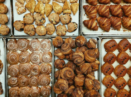 A variety of baked goods on trays, including pastries, cookies, and cinnamon rolls, arranged neatly.
