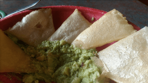 A red plate with crispy tortilla chips and a serving of guacamole.